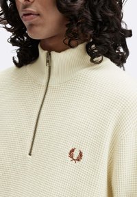 Maglione crema con zip e collo a costine, realizzato in tessuto testurizzato, con logo marrone ricamato sul lato sinistro del petto.