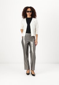Cardigan blanc avec fermeture à boutons, t-shirt noir, pantalon large en métal argenté, et escarpins noirs. Les accessoires comprennent des lunettes de soleil en forme de chat.