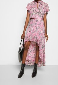 Vestido floral con mangas cortas y onduladas, dobladillo asimétrico, en tonos rosa y negro. Combinado con botas de tacón negras y un bolso negro.
