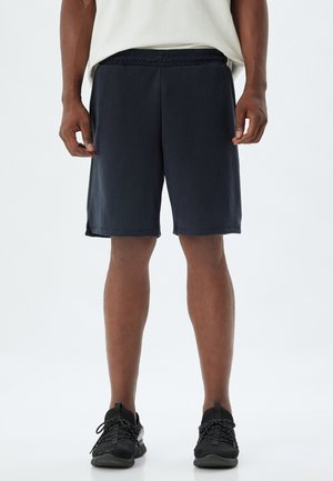 Marineblå atletiske shorts lavet af letvægtsstof med elastisk talje og sidelufter for nem bevægelse. Båret med sorte sneakers.