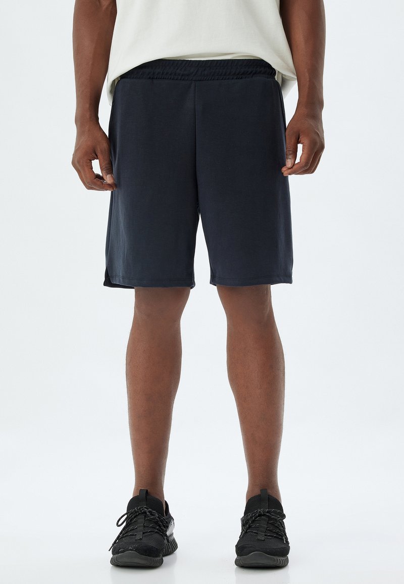 Marina atletiska shorts gjorda av lätt tyg med elastisk midja och sidofickor för enkel rörelse. Bärs med svarta sneakers.