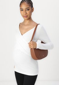 Witte wikkeltop, donkere broek, met een bruin leren handtas met een gouden accent. De top heeft een v-hals en een getailleerd ontwerp.