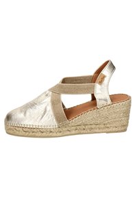 Metallic gold espadrille wedge with a canvas upper, elastic cross-strap, and woven jute sole. Closed back and open toe design.