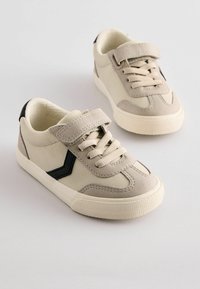 Beżowe zamszowe sneakersy z czarnym paskiem akcentującym, z sznurkami z przodu i rzepem. Teksturowana gumowa podeszwa. Prosty, sportowy design.