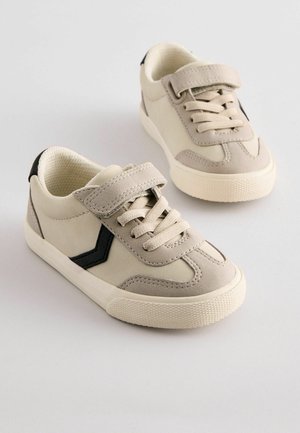 Beige mokkasiner av semsket skinn med svart aksentstripe, snøring foran og borrelåsrem. Teksturert gummisåle. Enkel, sporty design.