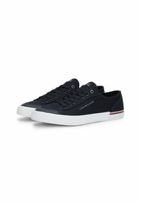 Zapatillas de lona navy con suelas de goma blanca. Las características incluyen seis ojales, diseño cosido y una raya de contraste en rojo y blanco en el talón.