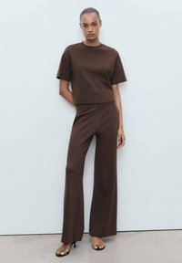 Brown knit short-sleeve top paired with matching high-waisted wide-leg trousers. Smooth texture and minimalistic design with no patterns.