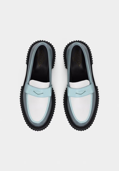 Ζευγάρι μοκασίνια με λευκά και γαλάζια δερμάτινα πάνω μέρη και μαύρες ραβδωτές σόλες, φωτογραφημένα από ψηλά πάνω σε λευκό φόντο.