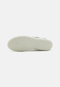 Fekete sneaker, texturált felsőrésszel, fehér gumitalppal, amelyen cikk-cakk mintázat található a tapadás érdekében. A talpon nincs látható márkajelzés.