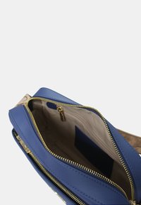 Borsa in pelle blu con hardware dorato, caratterizzata da un'apertura con zip e interni beige. Contiene una tasca con un accento blu navy.