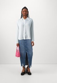Long-sleeved light blue blouse with a button front, paired with a denim skirt featuring a front slit and frayed hem. Holding a pink handbag.