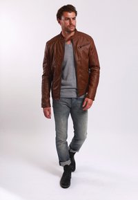 Schwarzlederjacke mit einer Reißverschlusstasche, kombiniert mit einem grauen Hemd, hellblauen Jeans und schwarzen Stiefeletten. Glatte Textur und taillierte Passform.