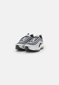 Sport shoes featuring a sleek design with a silver and black color scheme, textured fabric, curved stripes, and a contrasting pink accent.