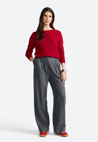 Pulover tricotat roșu, pantaloni largi gri și adidași roșii cu accente galbene. Mâneci lungi și croială lejeră. Textură de material neted.