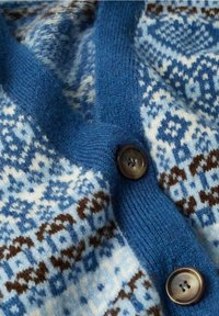 Tissu tricoté bleu et blanc avec des motifs géométriques, avec deux boutons foncés sur une couture côtelée bleue surélevée.