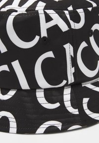 Chapeau seau noir avec de grandes lettres blanches imprimées sur le tissu, comportant des trous de ventilation cousus sur la calotte.
