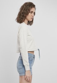 Kuttet lys grå sweatshirt med lange ermer, teksturert stoff og justerbar snøring i kanten. Sammen med lyseblå denimshorts.