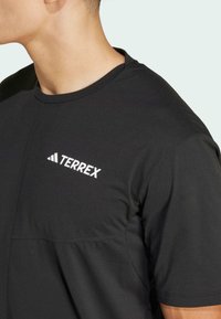 Zwarte sport T-shirt met korte mouwen, voorzien van een ronde halslijn en een wit "TERREX" logo op de linkerkant van de borst.