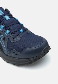Baskets de sport bleu foncé avec des matériaux en mesh et synthétiques, surface texturée, accents bleus et semelle extérieure en caoutchouc robuste.