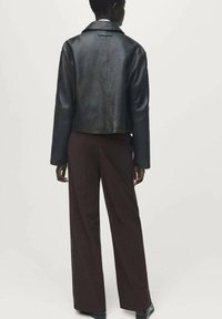 Zwart leren cropped jack met brede mouwen en een klassieke kraag, gecombineerd met donkere bruin hoge taille broeken. Gladde textuur, minimale details.