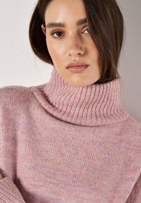 Helles rosa Rollkragensweatshirt aus weichem, strukturiertem Strickstoff mit geripptem Kragen und Bündchen, das ein dezentes, ineinander übergehendes Farbmuster aufweist.
