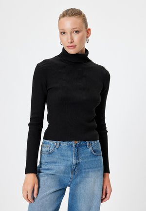 Schwarzer, gerippter Rollkragenpullover mit langen Ärmeln, kombiniert mit hochgeschnittenen blauen Jeans aus Denim. Glatte Textur und figurbetontes Design.
