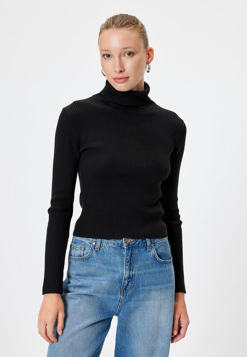 Maglione a collo alto nero a costine con maniche lunghe, abbinato a jeans in denim blu a vita alta. Texture liscia e design attillato.