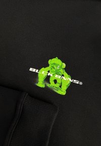 Zwarte stoffen sweatshirt met een groene graphic van een karakter en witte tekst die "BLCK BNNS" luidt. Het materiaal is zacht met een gladde textuur.