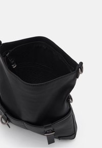 Černá kožená kabelka přes rameno s otevřeným vrchem, zobrazující vnitřní kapsu na zip a dekorativní kovové přezky na přední straně.