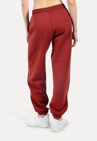 Czerwone dresy z miękkiego materiału, z elastyczną talią i ściągaczami na kostkach, w połączeniu z białymi tenisówkami.