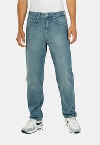 Jeans de mezclilla azul claro con un corte relajado, diseño de cinco bolsillos y un ligero desvanecimiento. Estilizados con una camiseta blanca y zapatillas blancas.