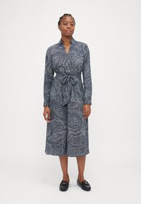 Vestito navy con motivo paisley, maniche lunghe e una cintura da annodare in vita. Il vestito ha un colletto ed è realizzato in tessuto leggero.
