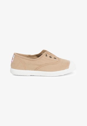 Chaussure beige en toile à enfiler avec semelle en caoutchouc blanche et bout en cap. Elle comporte deux œillets en métal et un petit patch logo sur le côté.