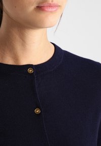 Granatowy sweter z dzianiny z okrągłym dekoltem i złotym guzikiem przy dekolcie. Teksturowany materiał o gładkim wykończeniu.