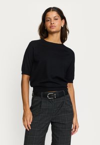 Pulover negru cu mâneci scurte, tricotat, cu decolteu rotund și tiv striat. Asortat cu pantaloni în carouri gri, cu talie înaltă și curea neagră.