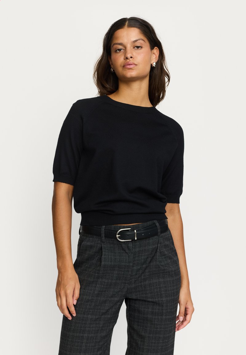 Pulover negru cu mâneci scurte, tricotat, cu decolteu rotund și tiv striat. Asortat cu pantaloni în carouri gri, cu talie înaltă și curea neagră.