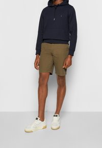 Marineblaue Kapuzenjacke, beigefarbene Shorts und weiße Sneakers. Die Jacke besitzt eine Fronttasche, während die Shorts ein flaches Design haben.