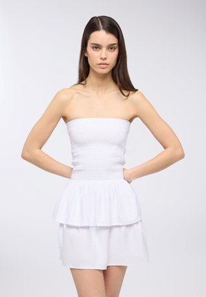 Abito bianco senza spalline con un corpino smock testurizzato e una gonna a strati con volant. Il tessuto ha un aspetto leggero e arioso.