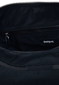 Interno di una borsa in tessuto nero con una tasca con zip e un'etichetta visibile "Desigual." Presenta una texture liscia e dettagli in cerniera argentati.