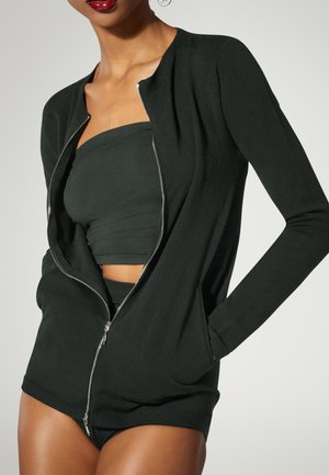 Giacca nera con zip frontale, maniche lunghe e una texture liscia. Sotto, è visibile un top bandeau scuro abbinato.