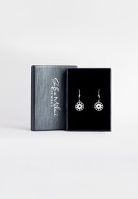 Silverörhängen med cirkulära hängande delar som har en stjärnexplosiondesign, visade i en svart sammetklädd låda med en silvertexturerad utsida.