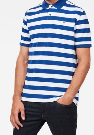 Homme portant un polo à manches courtes à rayures horizontales bleues et blanches avec col et deux boutons, associé à un jean foncé.