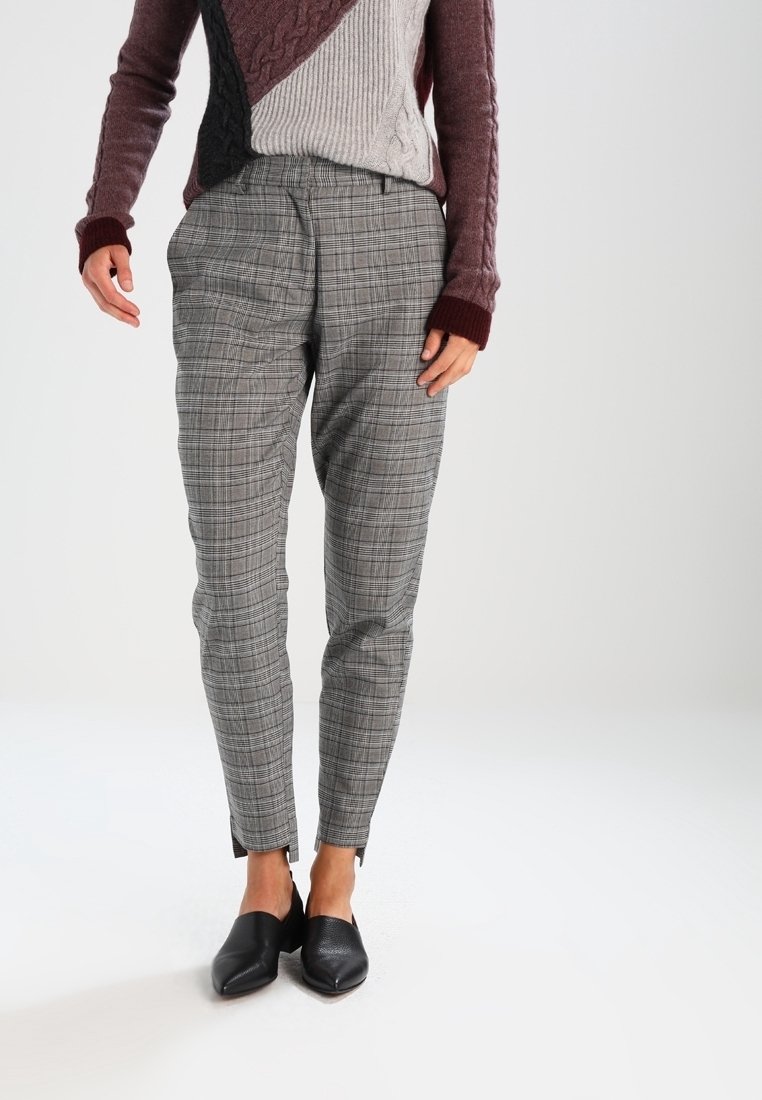 Grijze geruite broek met taps toelopende pijpen en twee zijzakken, gecombineerd met zwarte schoenen. De stof heeft een gladde textuur en een subtiele glans.