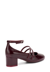 Chaussure en cuir bordeaux à talons carrés avec bride de cheville et double boucle. Bout rond et texture lisse avec une finition polie.