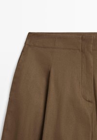 Bruine hoogmiddelrok die de tailleband, naden en subtiele plooien toont, met een gladde stof textuur op een witte achtergrond.