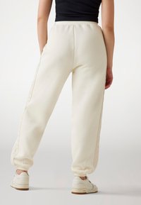 White sweatpants with a tapered fit, elastic cuffs, and side seam accents. Paired with white sneakers, texture appears soft and smooth.