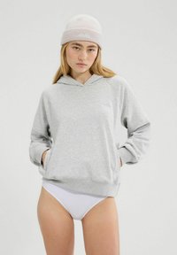 Grau Baumwoll-Hoodie mit einer Fronttasche und gerippten Bündchen. Kombiniert mit weißer Unterwäsche. Glatte Textur und entspannter Schnitt.