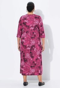 Maxikleid in Rosa mit schwarz-weißer floralem Paisleymuster, Dreiviertelärmel, runder Ausschnitt und fließender Silhouette. Flache schwarze Schuhe.