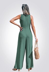 Mono sin mangas verde, con tela texturizada, piernas anchas y cierre de cremallera en la parte trasera, combinado con una bolsa tejida.