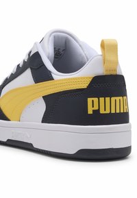 Sneaker noir et blanc avec des accents jaunes, présentant une tige en cuir lisse, un panneau latéral texturé et un logo "PUMA" bien en vue sur le talon.